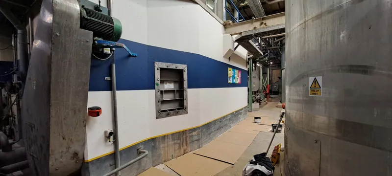 Blauw-witte hallenwand met een metalen luik, tussen de installaties.