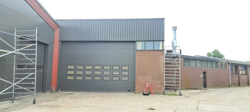 Bedrijfspand met een grijze sectionaaldeur en een rolsteiger ernaast.