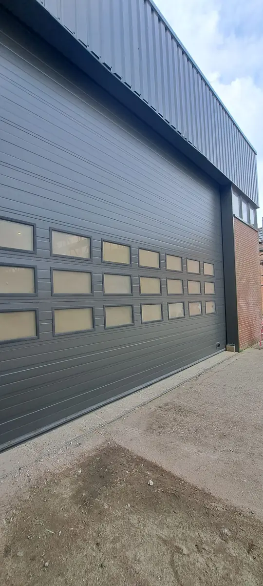 Dezelfde gevel en overheaddeur, afgewerkt in strak antracietgrijs.