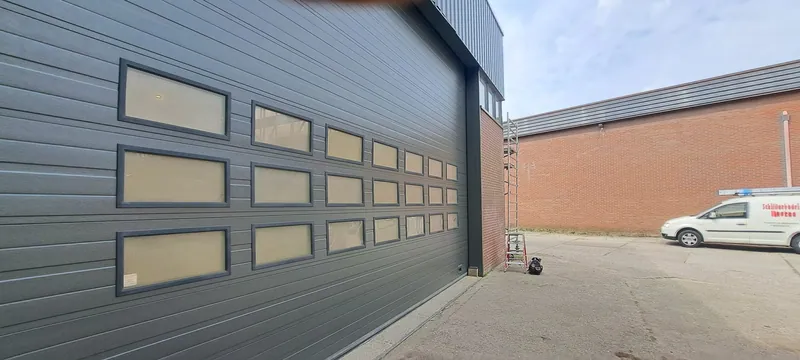 Brede antracietgrijze sectionaaldeur in de gevel van een bedrijfspand.