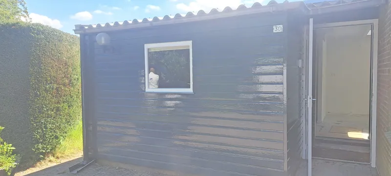 Antracietgrijze berging met een deur en een raam, na het schilderwerk.