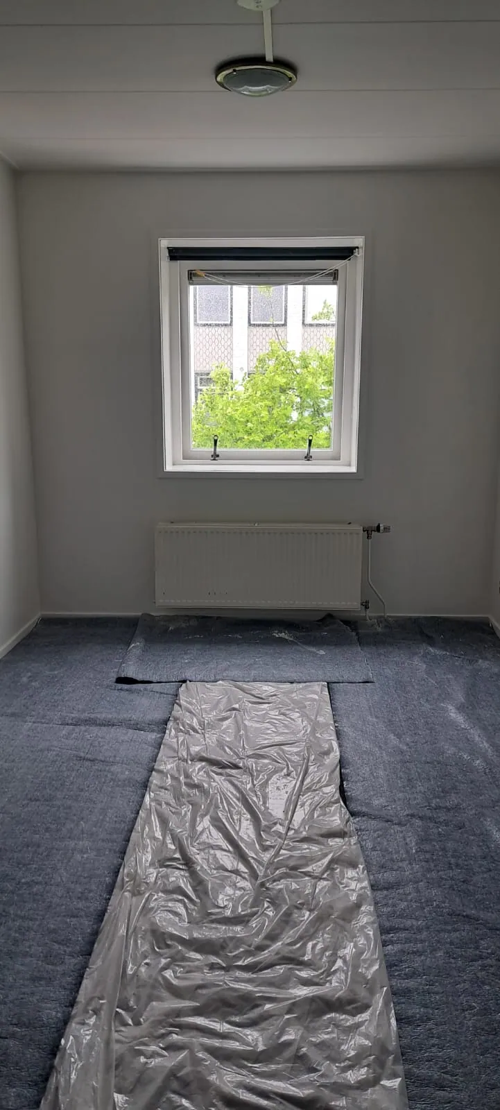 Leeggehaalde kamer, wit geschilderd, met dekzeil op de vloer.
