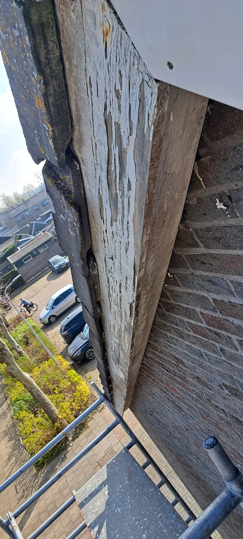 Verweerde houten boeidelen onder een dakrand, de verf is grotendeels weg.