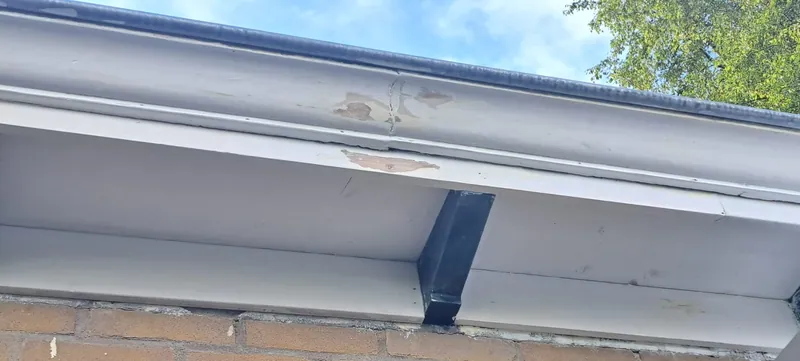 Witte dakgoot met een donkere console tegen een bakstenen gevel.