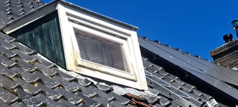 Witte dakkapel op een donker dak tegen een blauwe lucht.