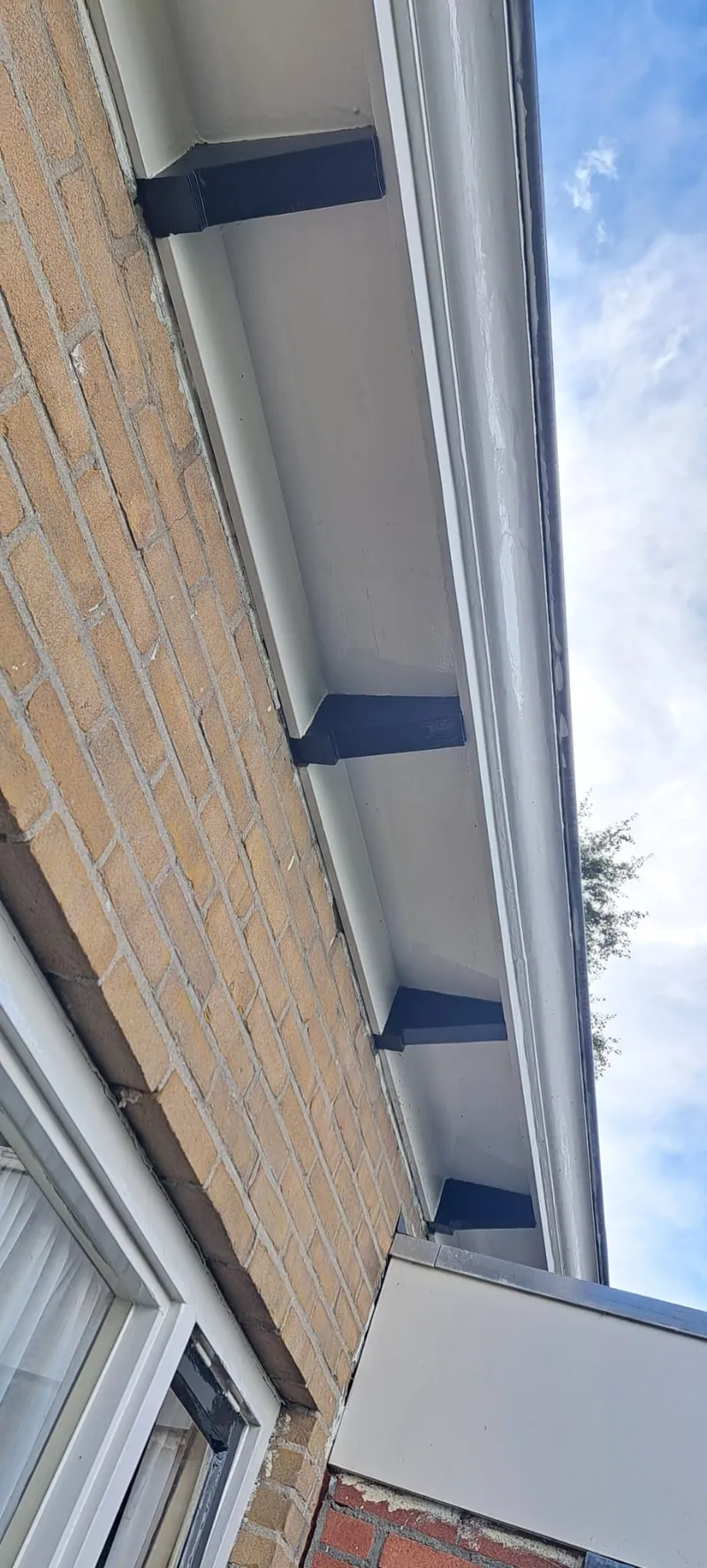 Blauw-wit dakoverstek langs een lichte bakstenen gevel.