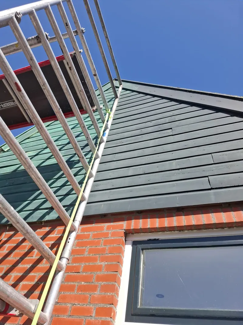 Dakoverstek boven een bakstenen gevel, met de steiger langs de dakrand.
