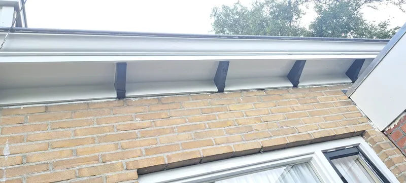 Wit dakoverstek met zwarte klossen boven een houten gevel.