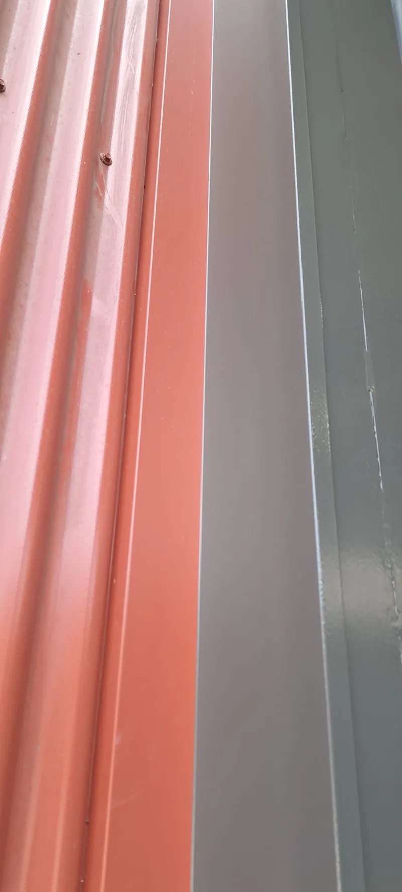 Detail van rode damwandbeplating naast een grijze gevelplaat.