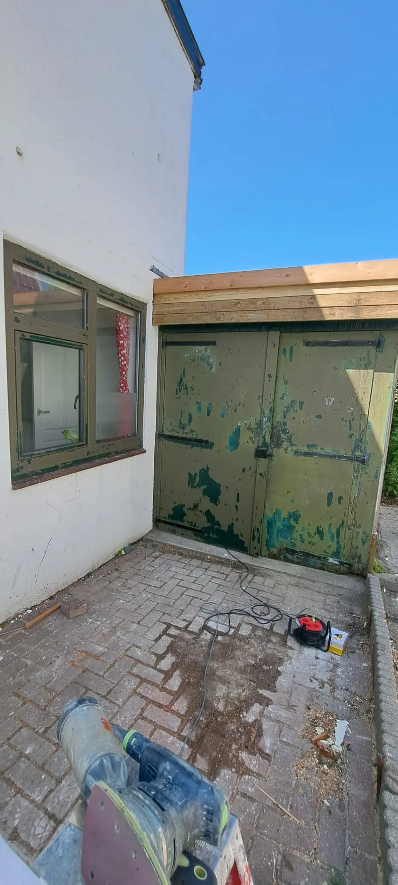 Groene garagedeuren en kozijn tijdens het werk, met de spullen op de stoep.