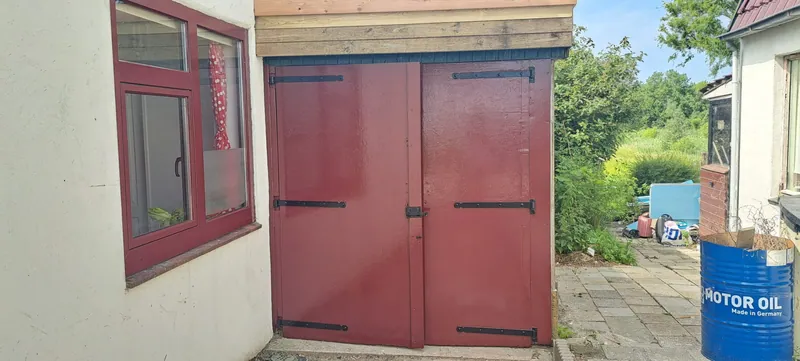 Dubbele garagedeuren en een raamkozijn, pas geschilderd in diep roodbruin.