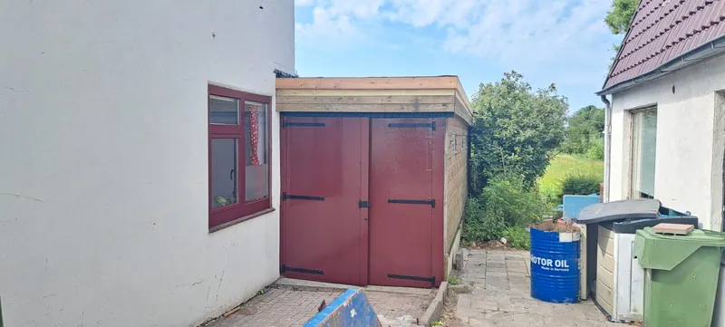 Rode garagedeuren en een rood kozijn in een witgepleisterde gevel.