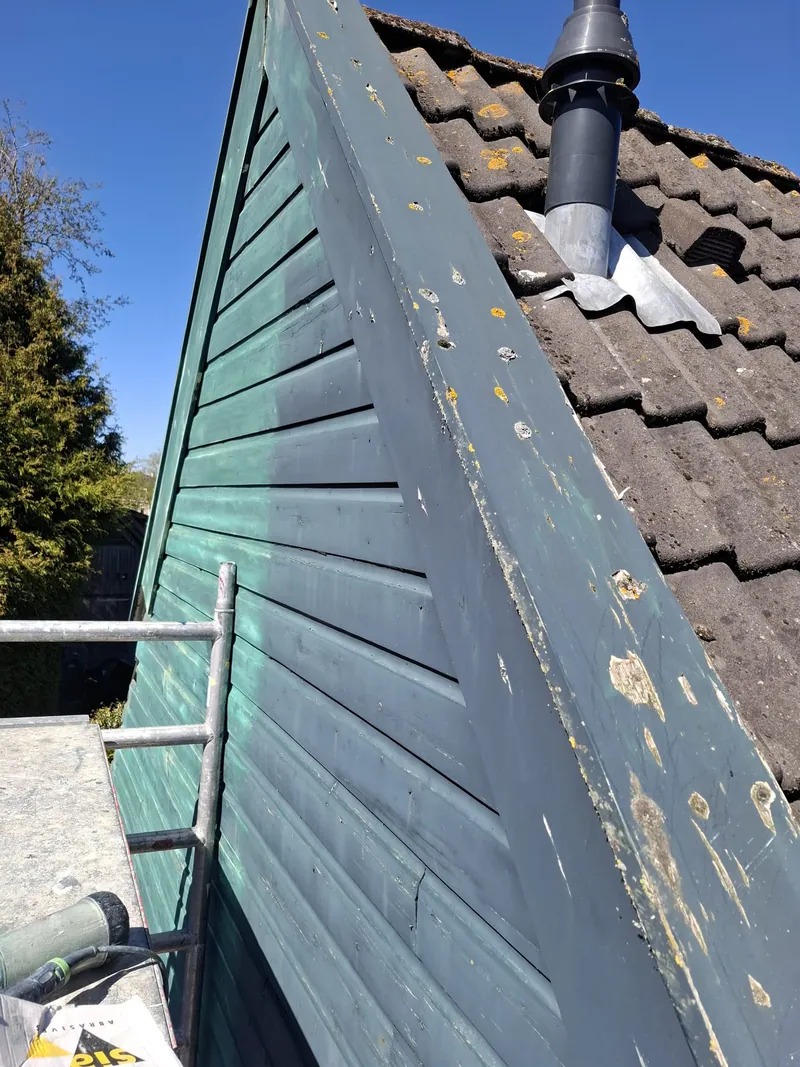 Donkergroene houten gevel onder een pannendak, met bladderende verf.