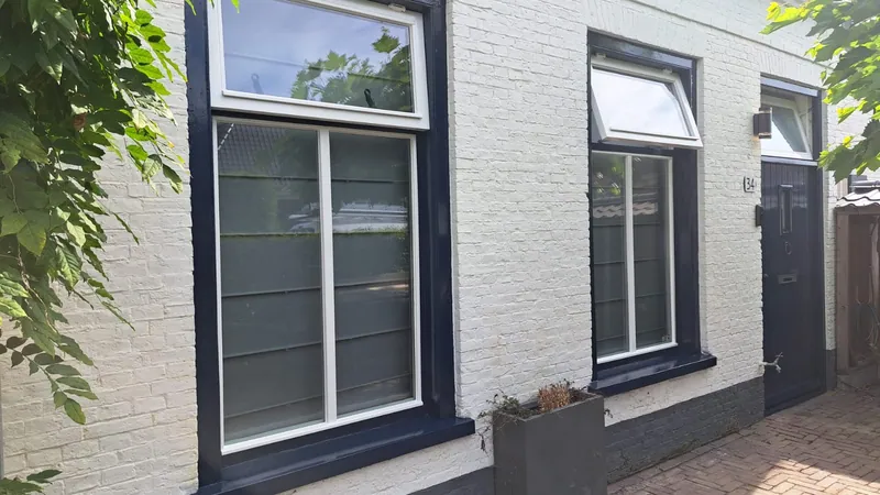 Witte gevel met donkerblauwe kozijnen langs een tuinpad.