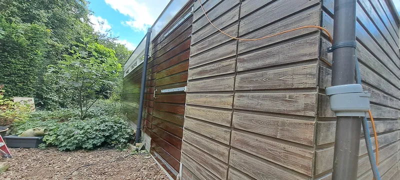 Blanke houten gevelbekleding in een tuin, met de regenpijp ernaast.