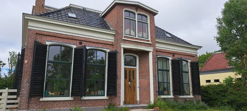 Herenhuis van rode baksteen met zwarte luiken, lichte kozijnen en een houten voordeur.