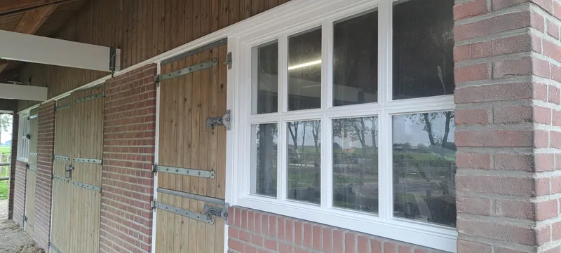 Houten wand met een rij witte kozijnen onder een overkapping.