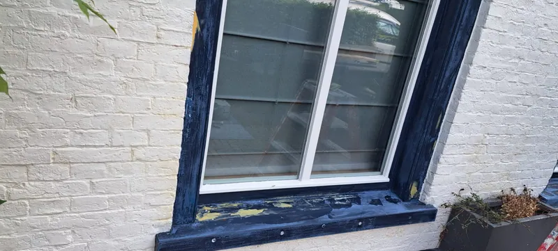Blauw kozijn in een witte gevel tijdens het werk, met plamuur op de onderdorpel.