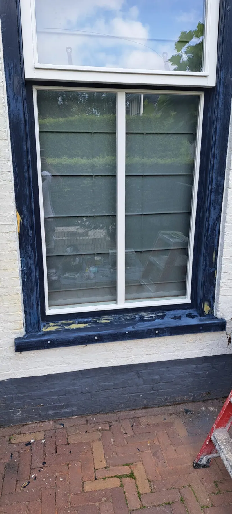 Donkerblauw kozijn met een wit raam boven een bakstenen stoep.
