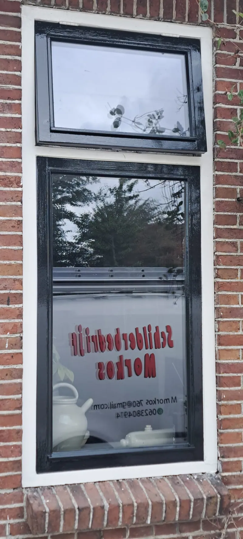 Zwart kozijn in een bakstenen gevel, met de raamsticker van het schildersbedrijf.
