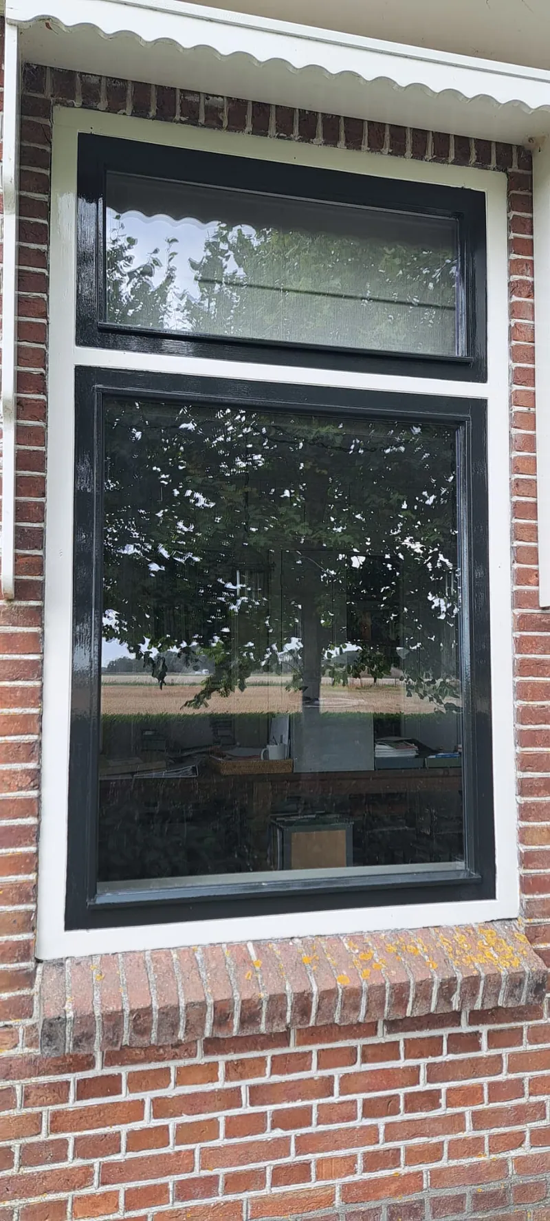 Zwart kozijn onder een wit dakoverstek in een bakstenen gevel.