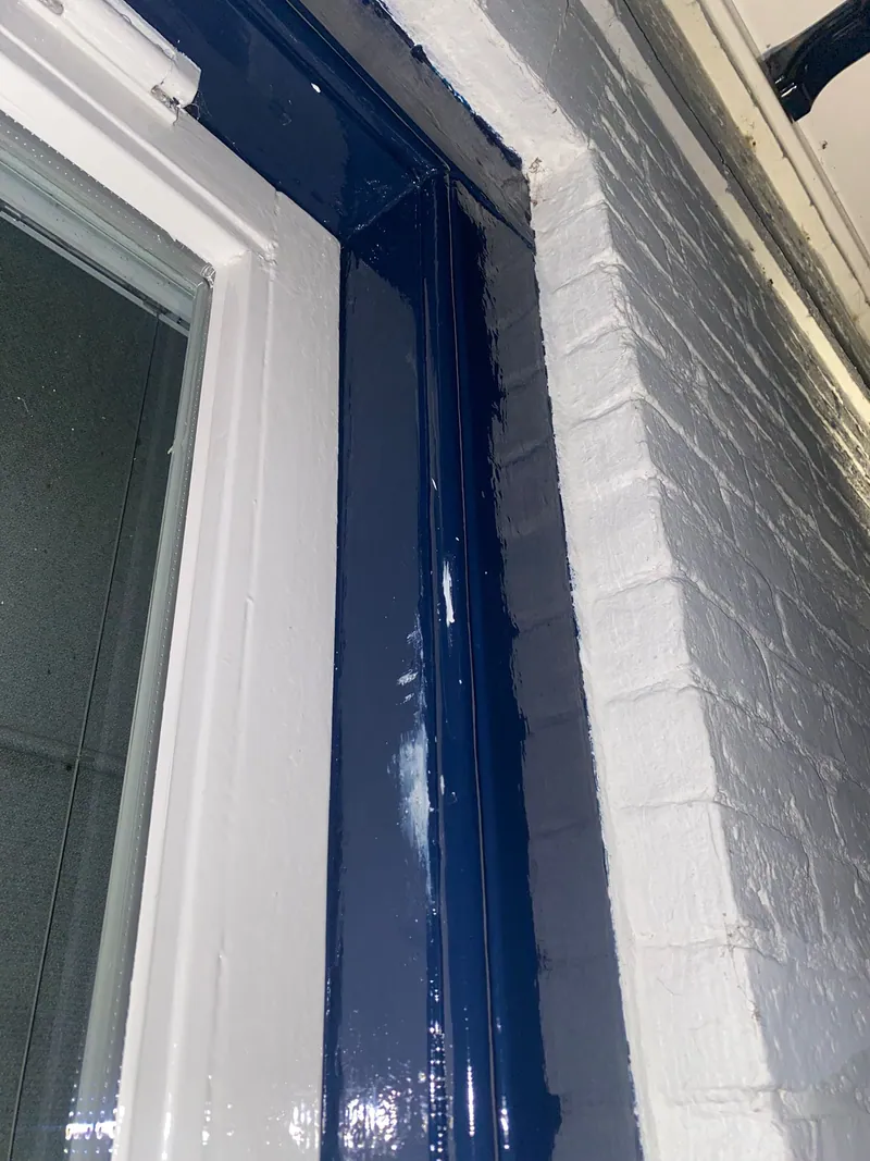 Hoek van een donkerblauw kozijn met verse verf tegen een witte muur.