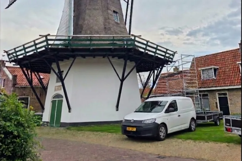 De witgeschilderde molen van Stiens met de bus en aanhanger van Schildersbedrijf Morkos ervoor.