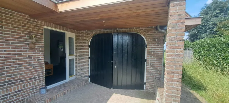Overkapping met zwarte deuren tussen bakstenen kolommen.