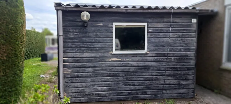 Verweerde houten schuur met een klein raampje, voor het schilderwerk.