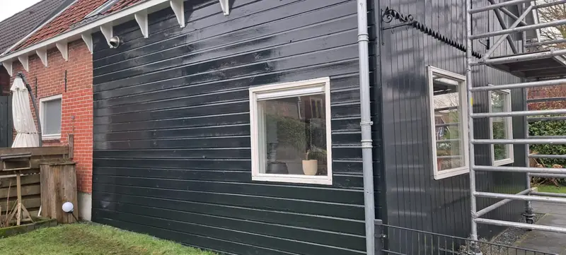 Dezelfde houten aanbouw, nu diep zwart geschilderd met witte kozijnen.