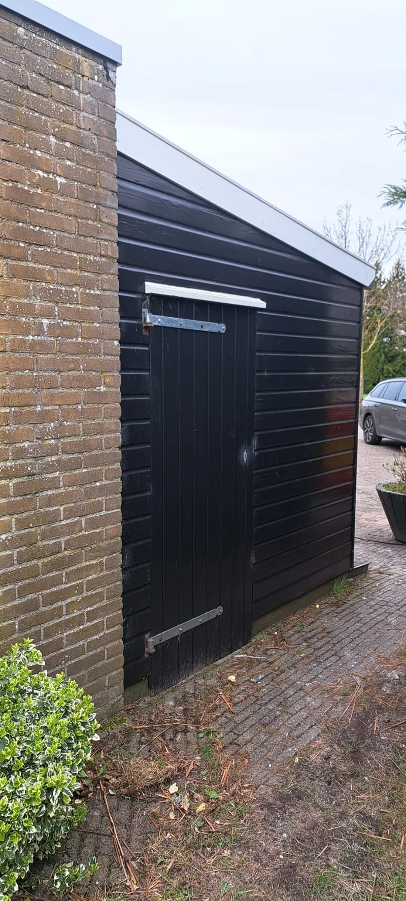 Houten schuur met een strak zwarte gevel en een donkere deur.