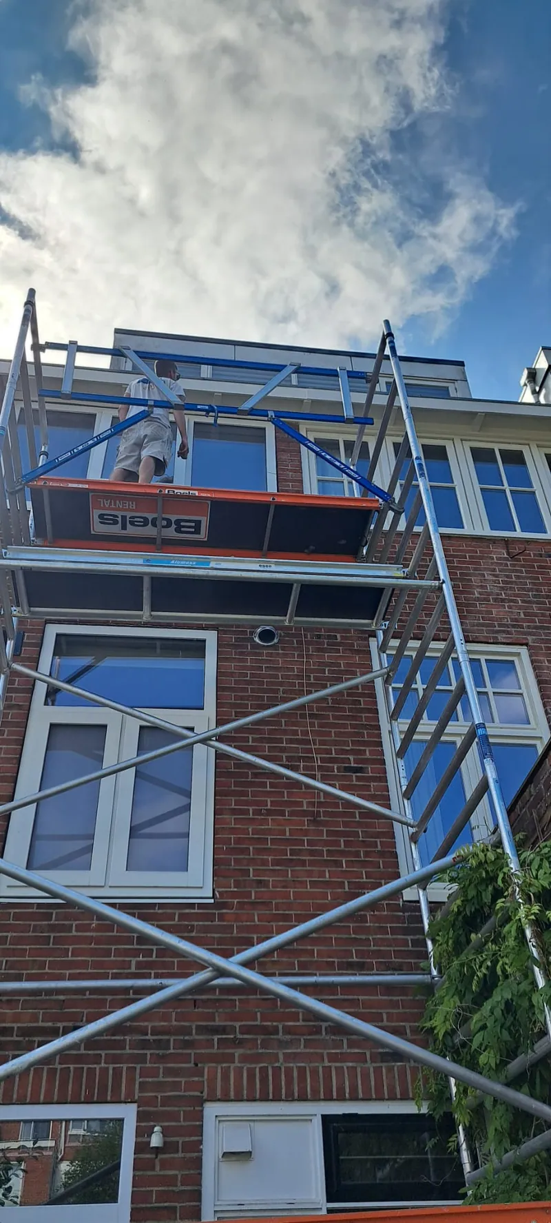Rolsteiger tegen een bakstenen woning met witte kozijnen en een dakkapel.