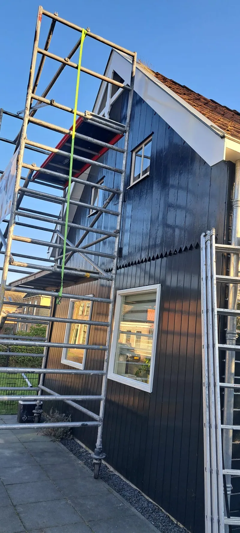 Steiger langs een zwart geschilderde houten gevel tijdens het werk.