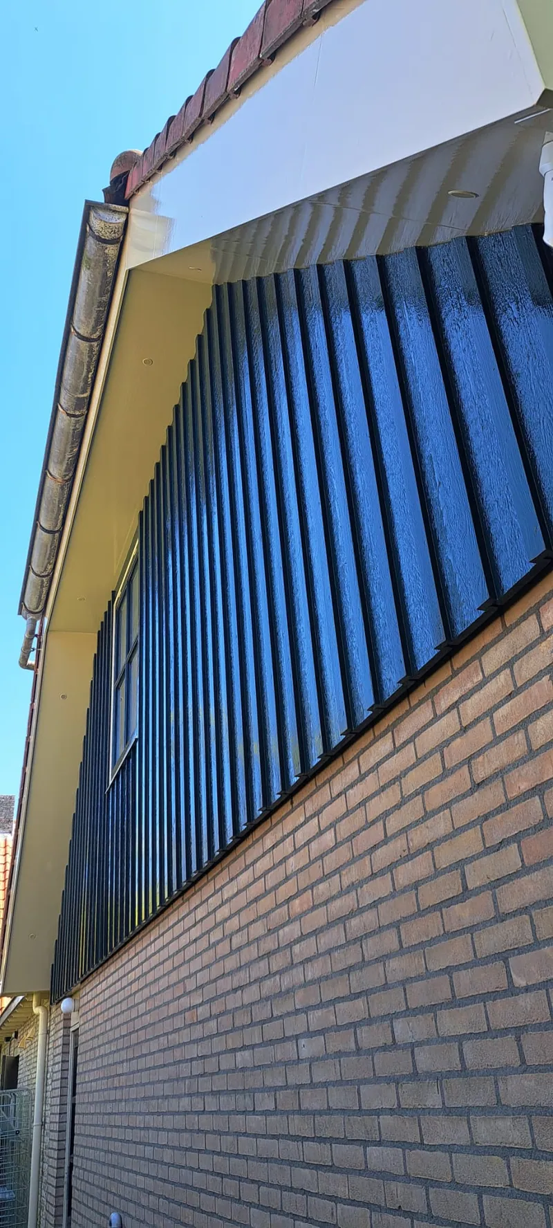 Blauwe houten topgevel met een wit boeiboord boven een lichte bakstenen gevel.