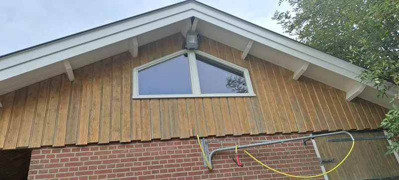 Houten topgevel met een raam boven een bakstenen gevel.