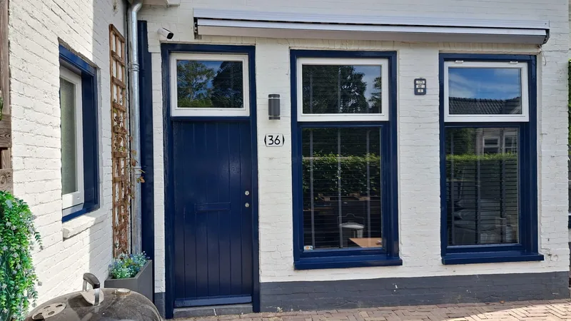 Witte gevel met een donkerblauwe voordeur en donkerblauwe kozijnen.