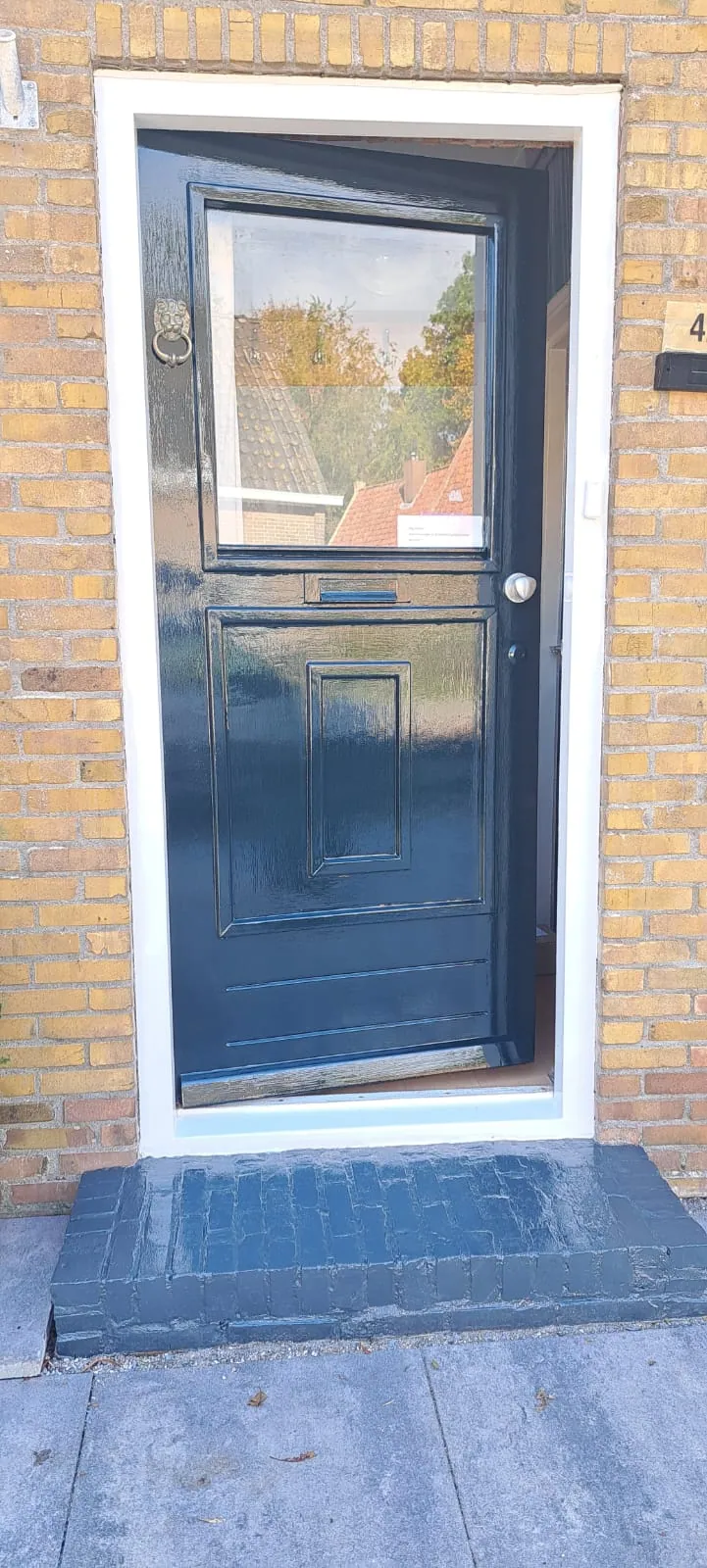 Donkerblauwe voordeur met bovenlicht in een wit kozijn.