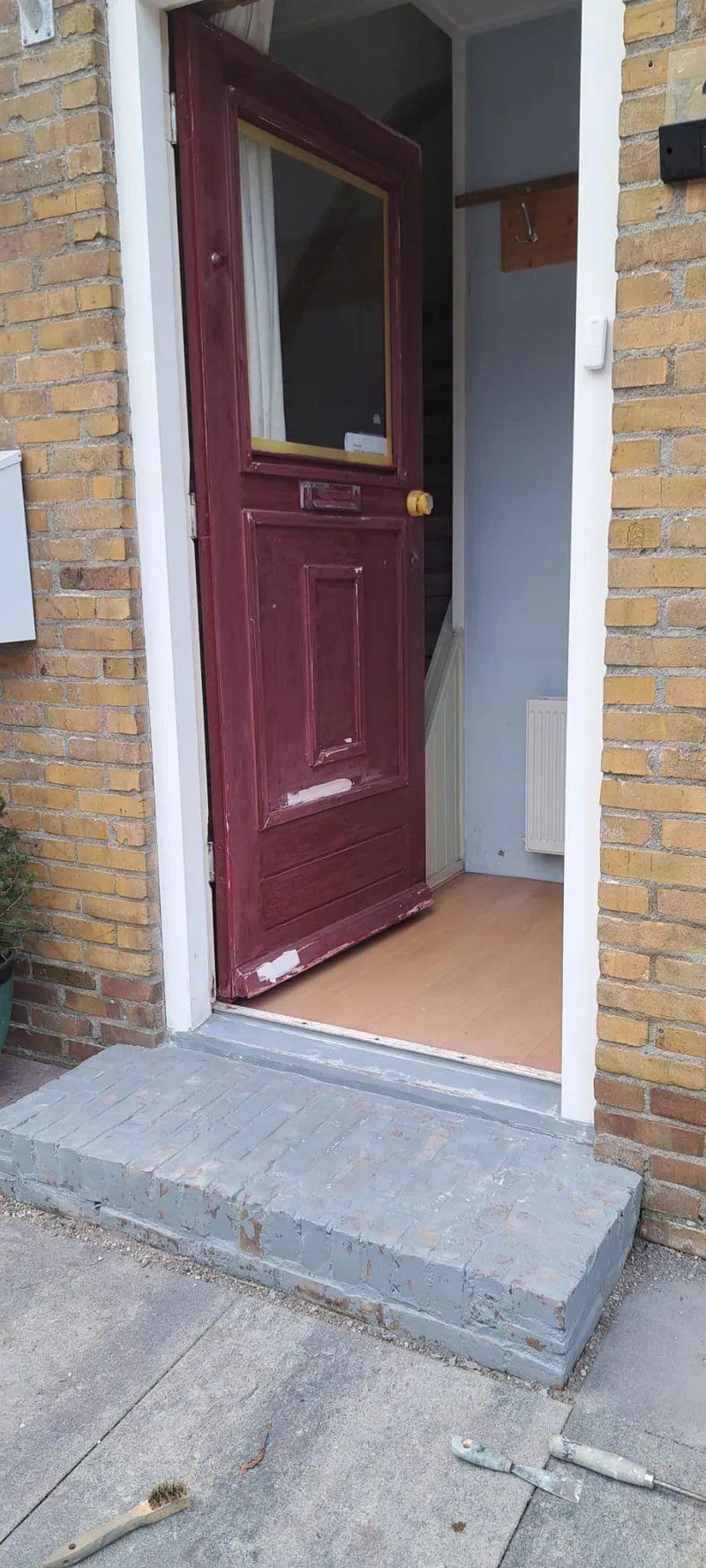 Donkerrode voordeur met een wit kozijn en een nieuwe hardstenen drempel.