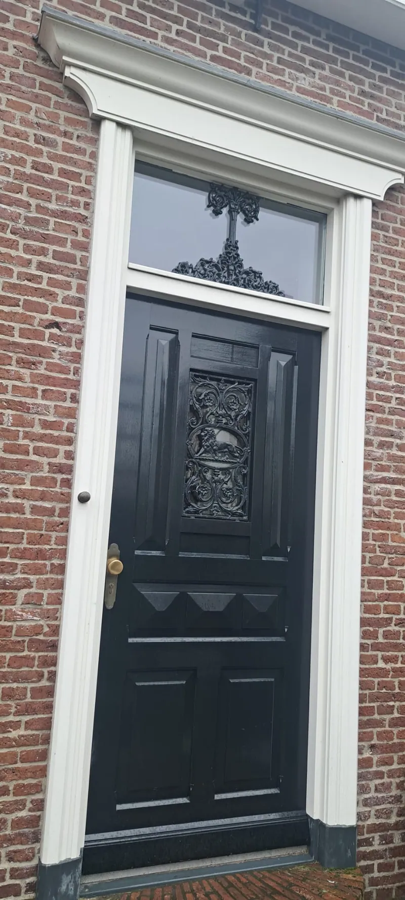 Zwarte paneeldeur met glas-in-lood bovenlicht in een bakstenen gevel.