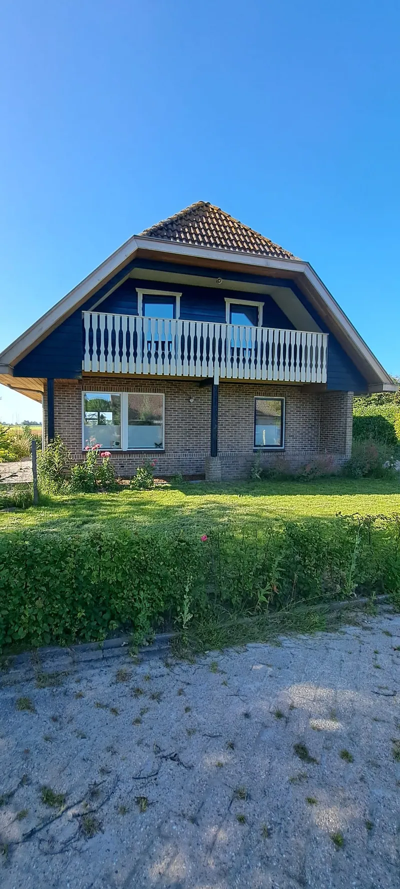 Vrijstaande woning met een balkon en een donkere houten gevel.