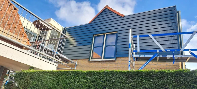 Woning met blauwgrijze houten gevelbekleding, met de steiger er nog tegenaan.