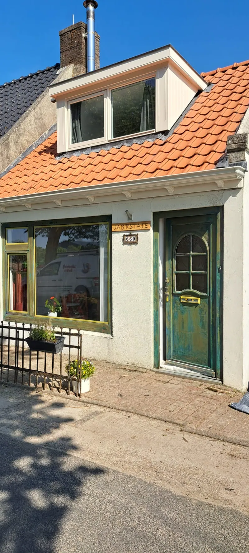 Woning met groene voordeur en groene kozijnen onder een oranje pannendak.