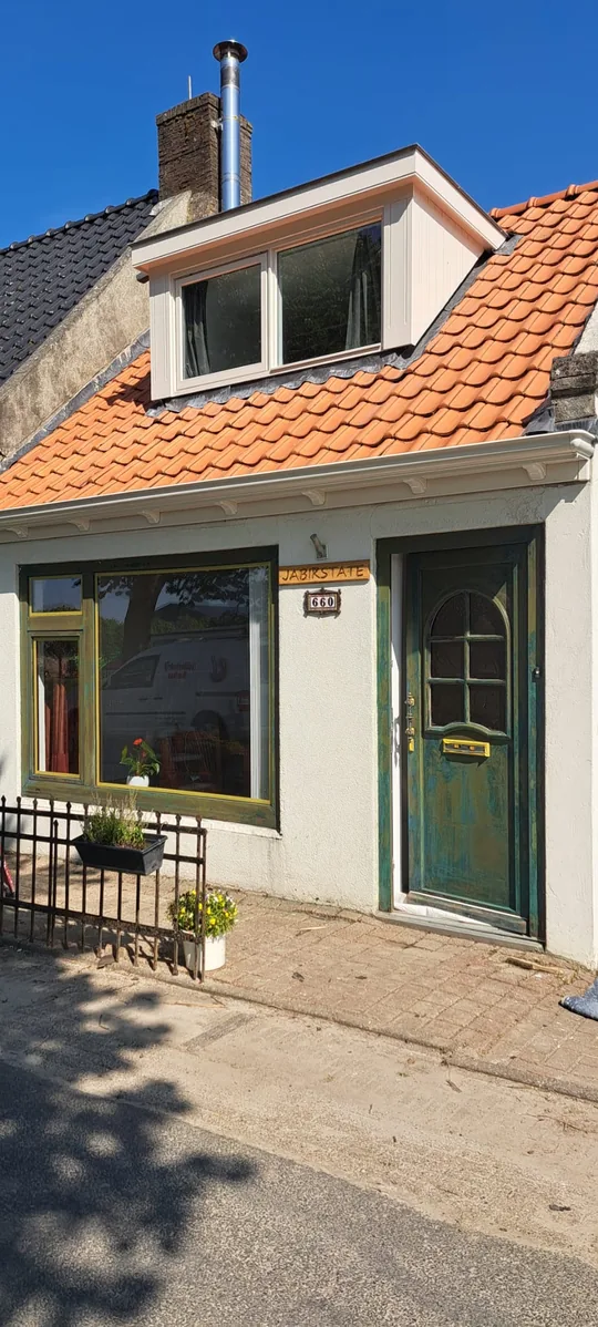 Woning met een groene voordeur en groene kozijnen onder een oranje pannendak.