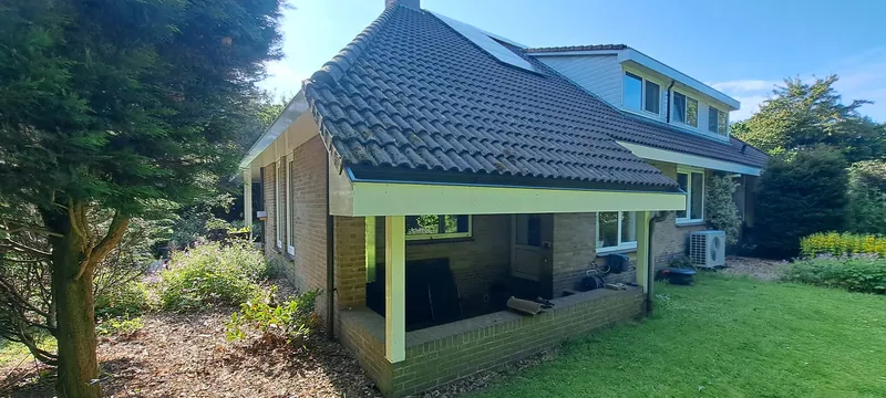 Woning met een overkapping en lichte kozijnen, gezien vanuit de tuin.