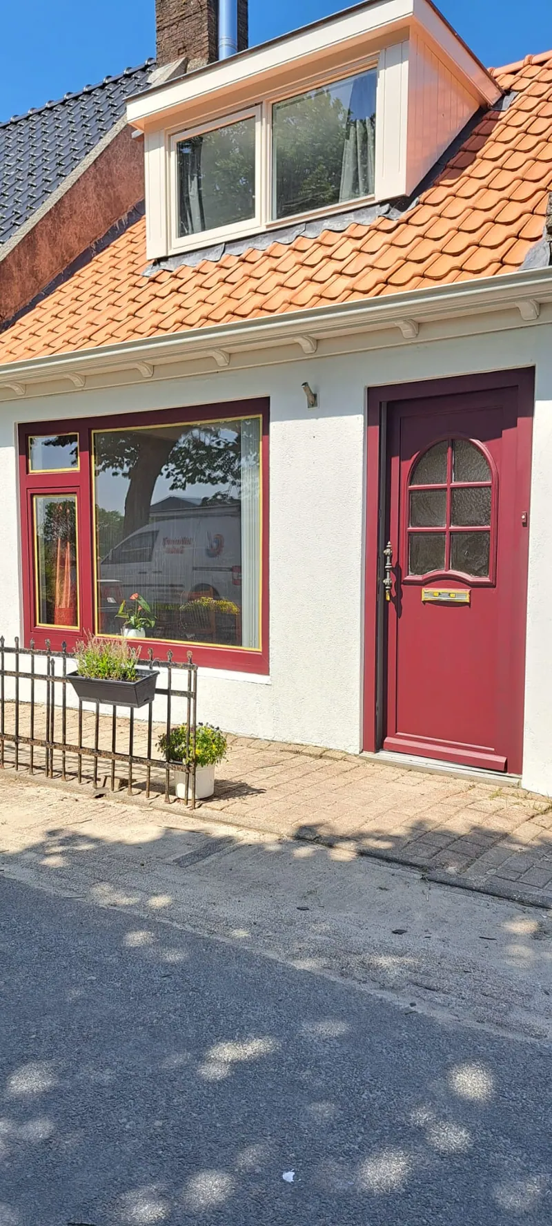 Dezelfde woning van opzij: rode voordeur, rode kozijnen, witte gevel.