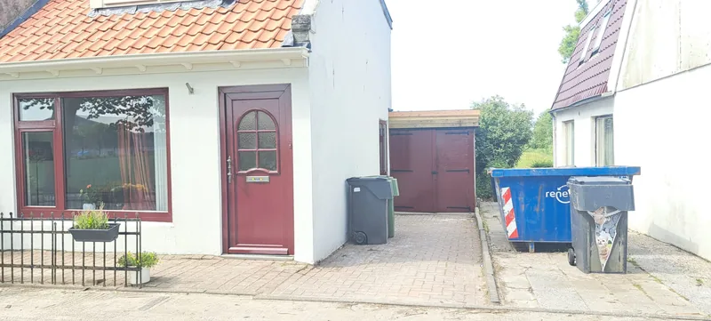 Witte woning met een rode voordeur, met op de achtergrond de rode garagedeuren.