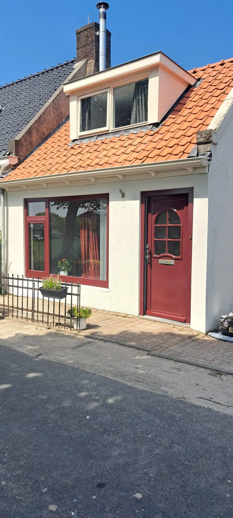 Woning met een pas geschilderde rode voordeur en rode kozijnen onder een oranje pannendak.