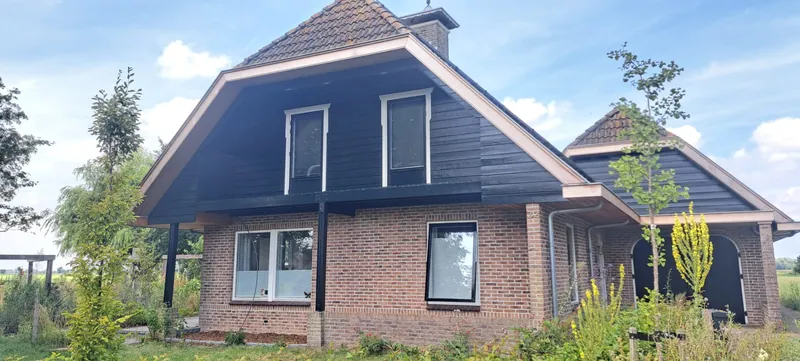 Vrijstaande woning met zwarte gevelbekleding en witte kozijnen.