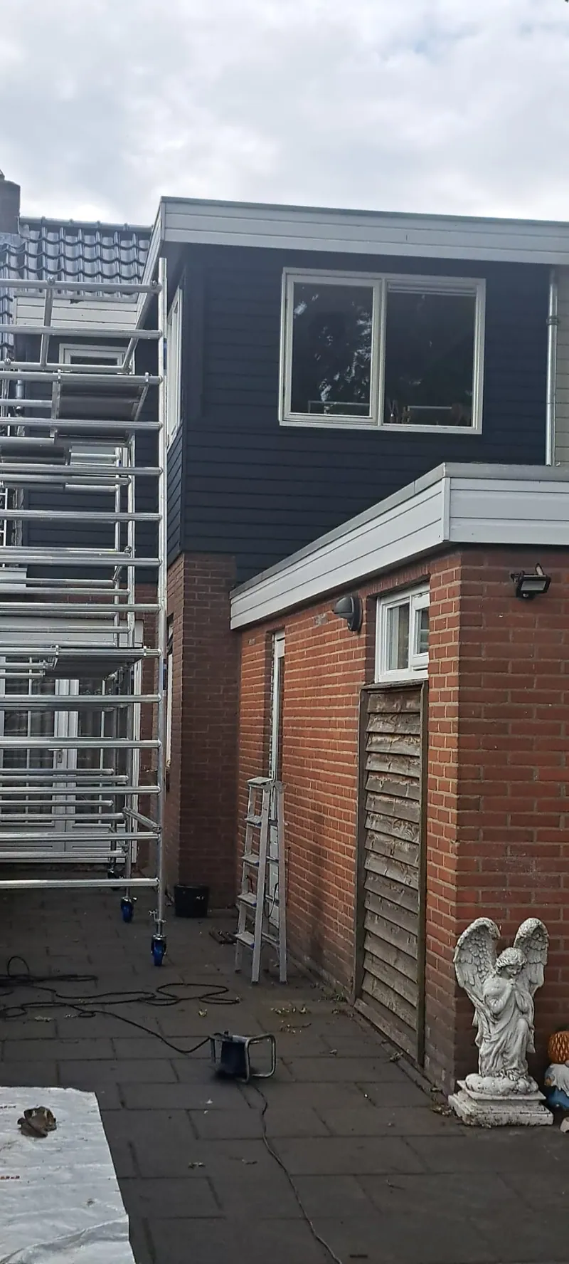Antracietgrijze zijgevel van een woning met de steiger nog tegen de bakstenen voorgevel.