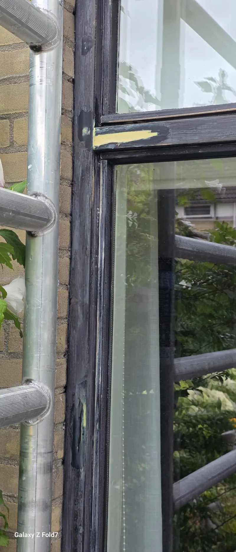 Detail van een zwarte houten gevel met een wit kozijn, achter de steigerbuizen.